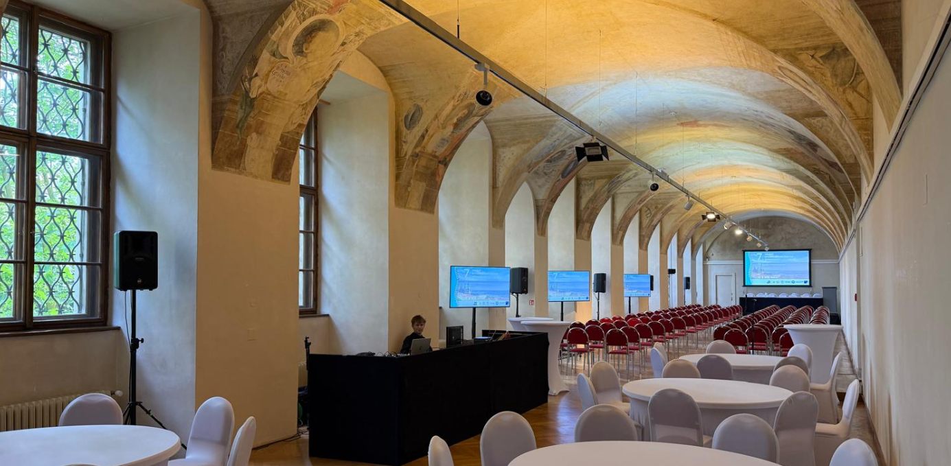 Historický klenutý sál s rozestavěnou konferenční technikou a obrazovkami